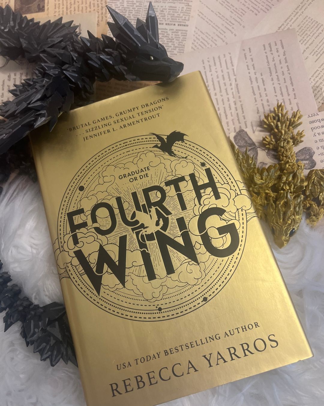 Fourth Wing by Rebecca Yarros, with its gold cover surrounded by dragon figurines and book pages, capturing the dark academia books aesthetic without being a true dark academia novel.